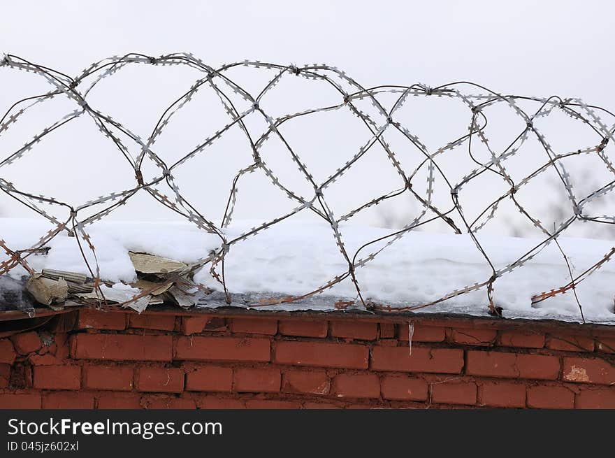 A brick fence with snow and barbed wire on top. A brick fence with snow and barbed wire on top