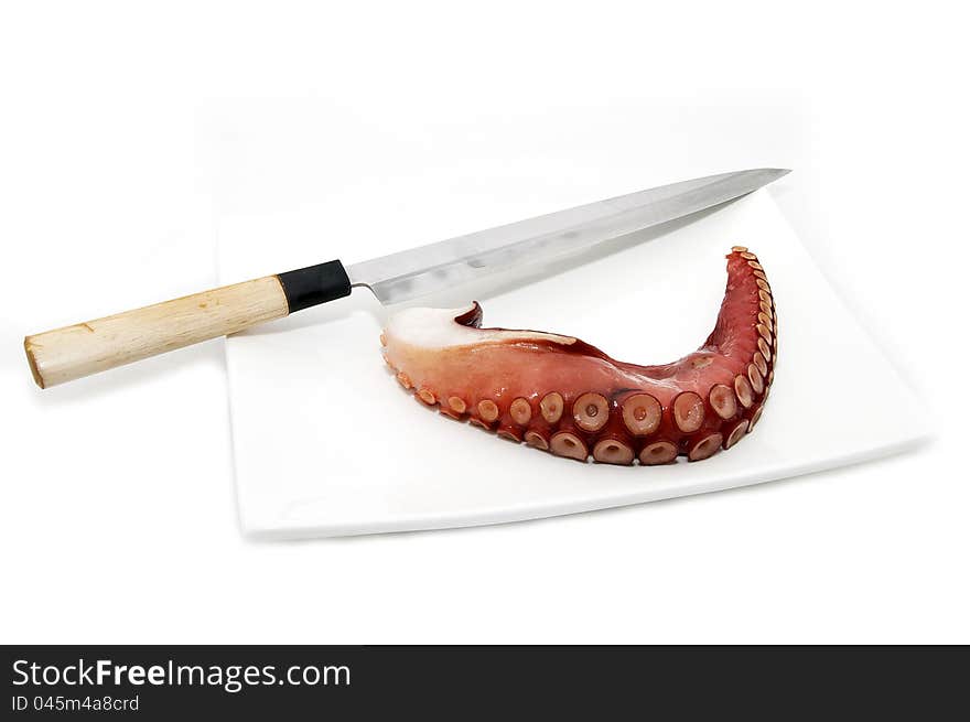 A piece of octopus on a plate and a knife on a white background