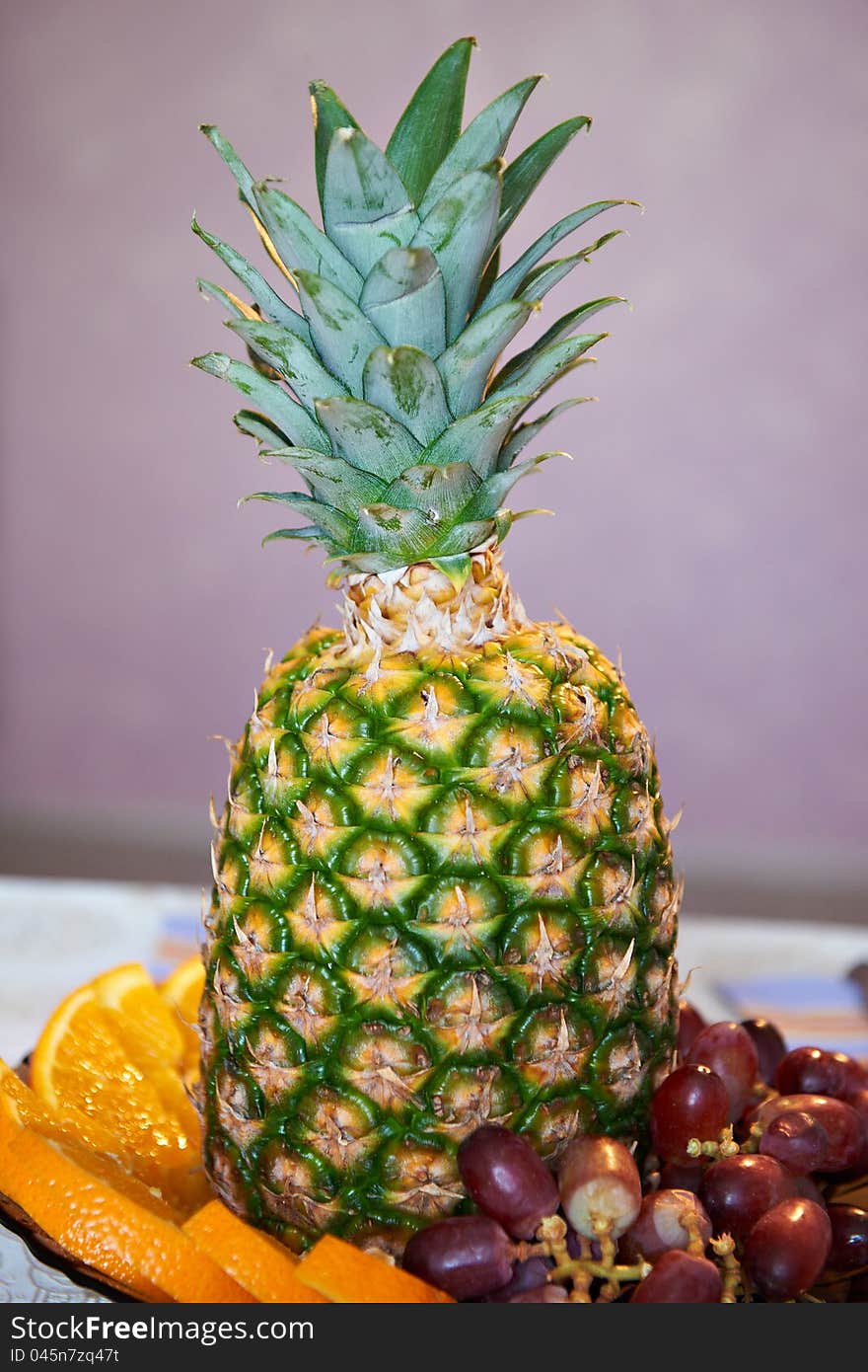 Pineapple with slices of oranges and grapes on table