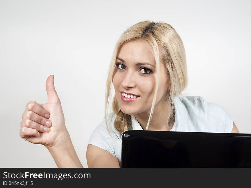 Beautiful happy girl sitting at a laptop computer and displays ok on the background of