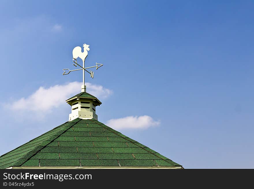 Rooster weather vane on roof and blue sky background