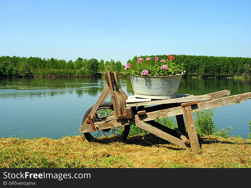 Old wooden wheel barrow with flowers close to river