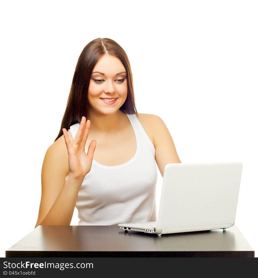 The young woman communicates  behind a table with the laptop on a white background. The young woman communicates  behind a table with the laptop on a white background