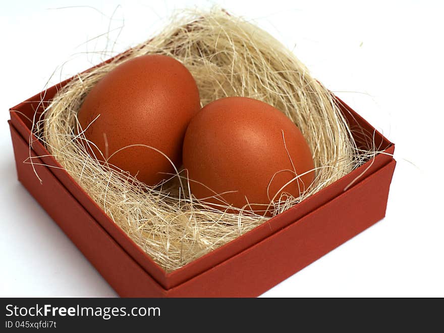 Two fresh brown eggs and some straw in a brown cardboard box on a white background. Two fresh brown eggs and some straw in a brown cardboard box on a white background