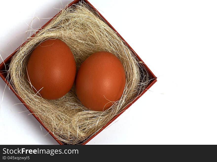 Two fresh brown eggs and some straw in a brown cardboard box on a white background. Two fresh brown eggs and some straw in a brown cardboard box on a white background