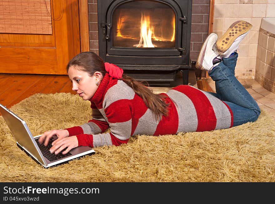 Girl with laptop lying on the carpet near the fireplace, and heated. Girl with laptop lying on the carpet near the fireplace, and heated