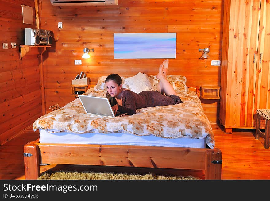 Girl with laptop lying on the bed in a rustic house and sends the mail to friends. Girl with laptop lying on the bed in a rustic house and sends the mail to friends