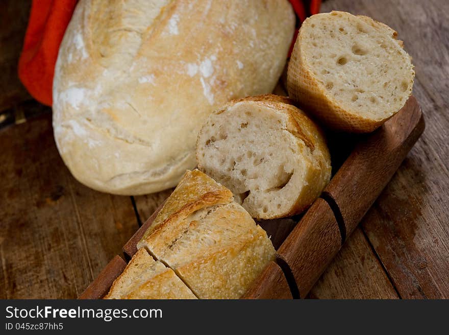 Freshly baked baguette sliced on a wooden bread cutting tray.  There is a second loaf of bread in the background. Freshly baked baguette sliced on a wooden bread cutting tray.  There is a second loaf of bread in the background.