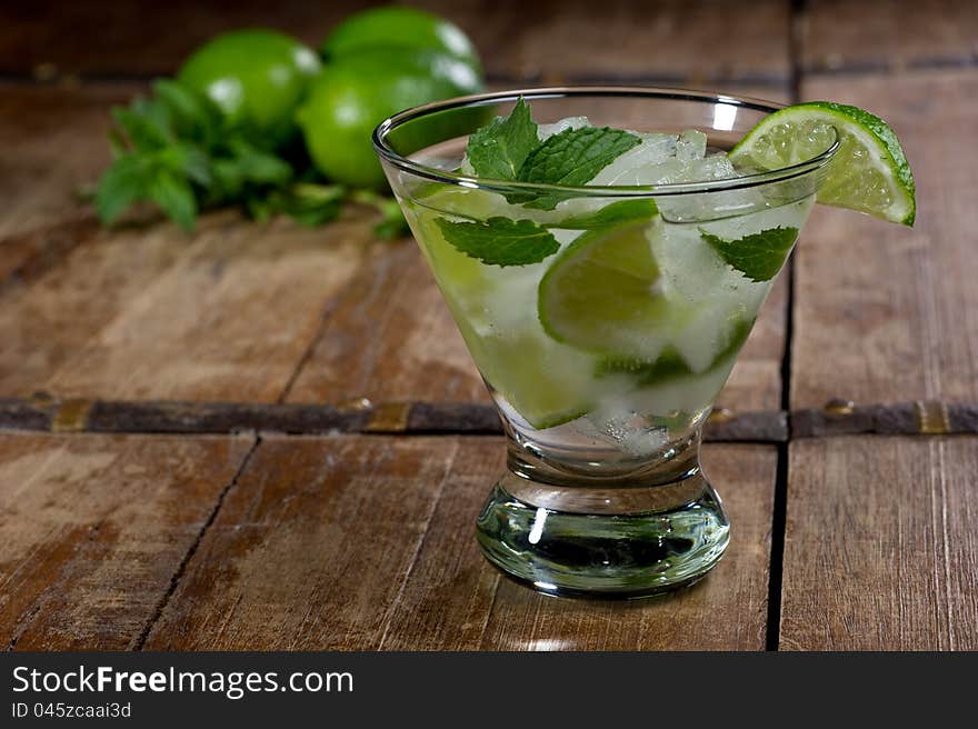 Fresh mojito in a lowball glass on a rustic table garnished with limes and mint leaves. Fresh mojito in a lowball glass on a rustic table garnished with limes and mint leaves.