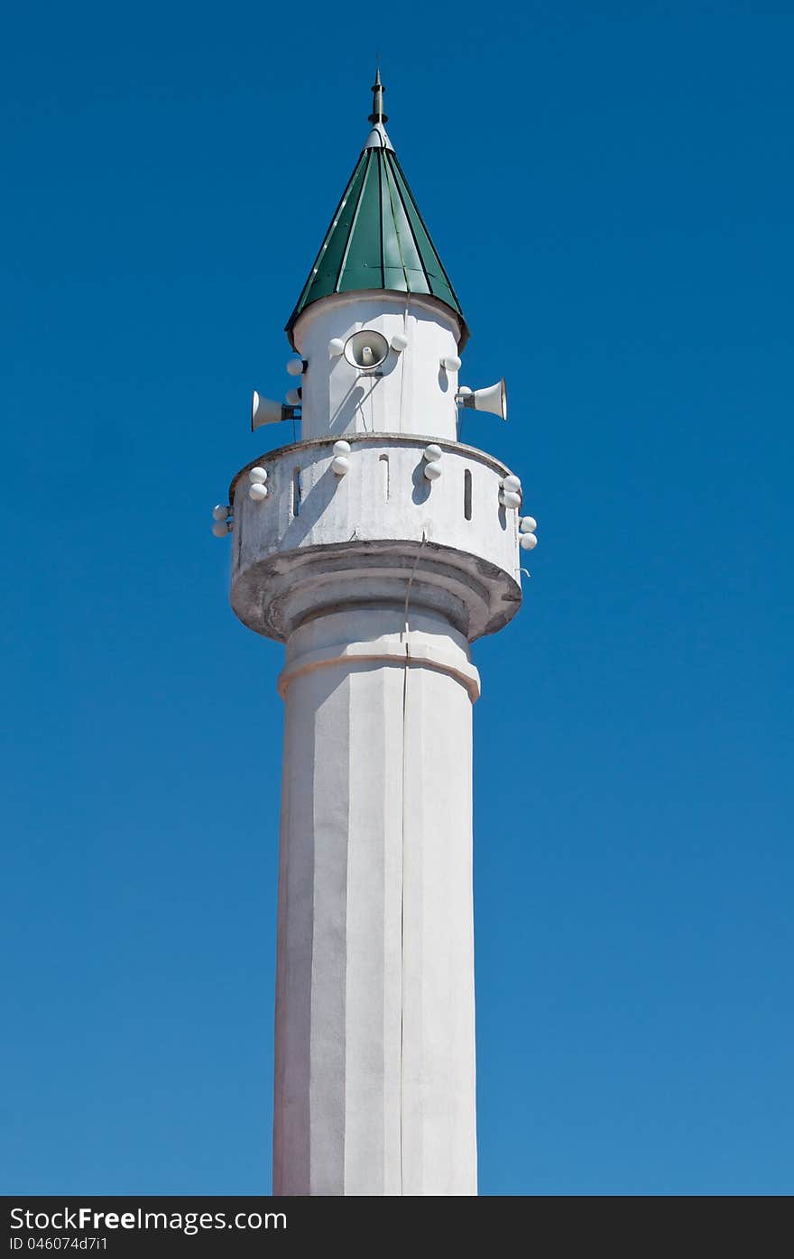 Small white minaret with green roof on blue sky