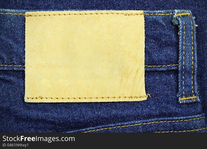 Blank leather jeans label sewed on a blue jeans, used as background for your text.