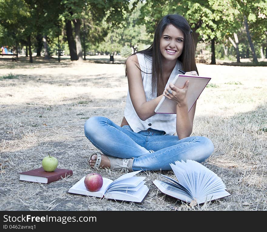 Young woman sitting on the grass and holding notebook photographed in  park. Young woman sitting on the grass and holding notebook photographed in  park