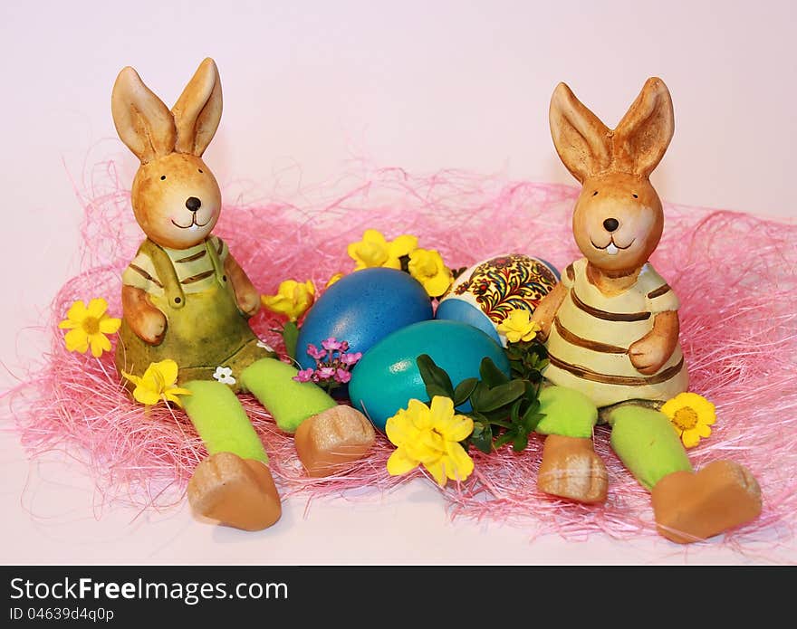 Toy rabbits are sitting near the dyed Easter eggs on a pink background. Toy rabbits are sitting near the dyed Easter eggs on a pink background