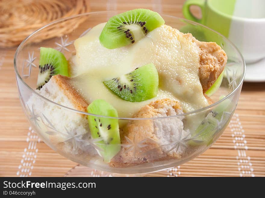 Dessert with slices of sponge cake, sweet cheese sauce and  kiwi in glass bowl on table. Dessert with slices of sponge cake, sweet cheese sauce and  kiwi in glass bowl on table