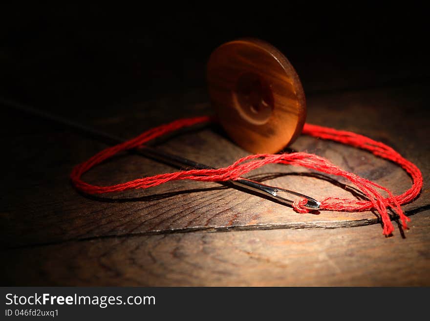 Sewing concept.Closeup of button and needle with thread on dark wooden background. Sewing concept.Closeup of button and needle with thread on dark wooden background