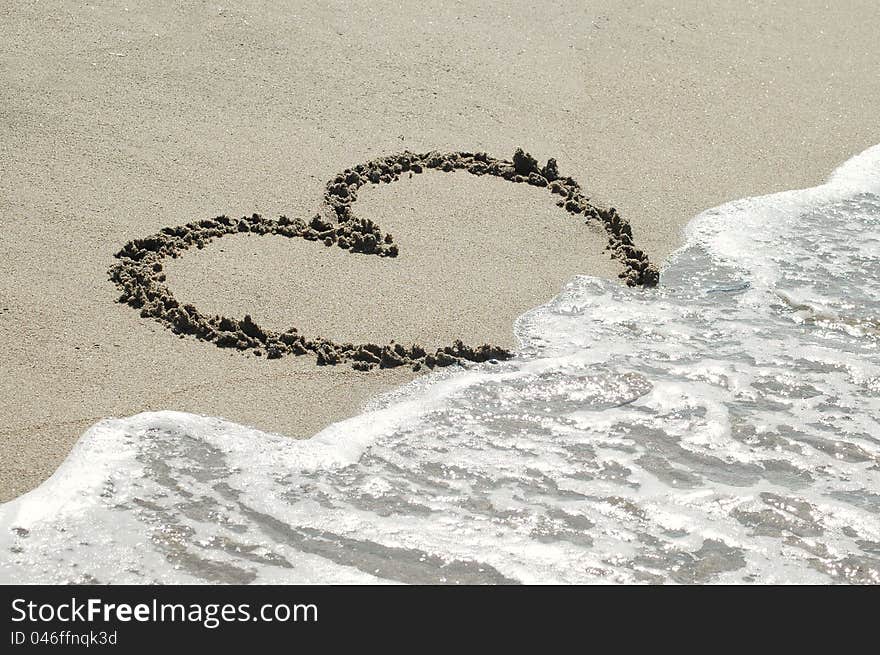 Handwritten heart on sand with wave approaching