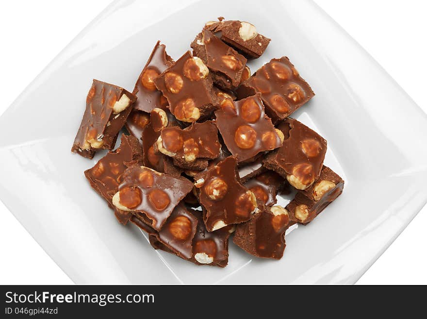 Broken chocolate pieces with nuts on white plate, top view, isolated. Broken chocolate pieces with nuts on white plate, top view, isolated