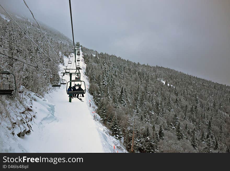 Ski lift ride takes skiers to the top of a snowy mountain among evergreen trees. Ski lift ride takes skiers to the top of a snowy mountain among evergreen trees.