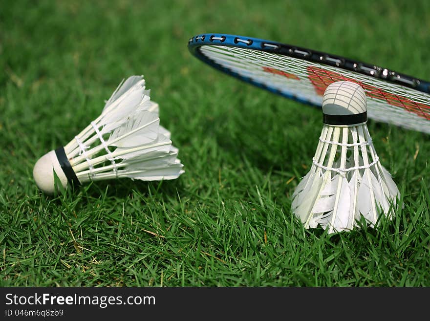 Two shuttlecocks and badminton racket lying on the grass. Two shuttlecocks and badminton racket lying on the grass