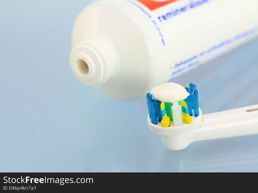 Toothpaste and a new electronic toothbrush head on a shiny blue background