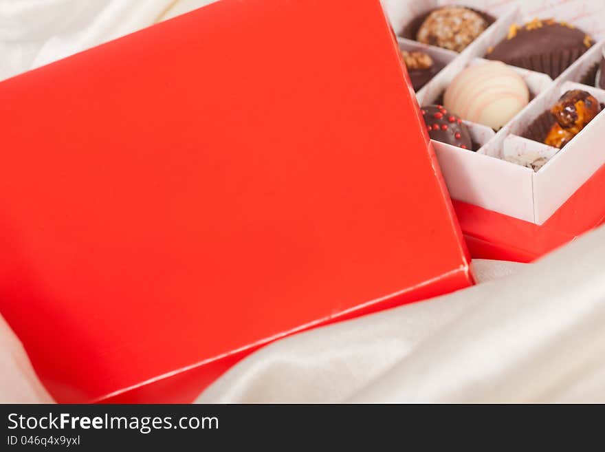 Red box of sweet handmade chocolates on white satin background. Red box of sweet handmade chocolates on white satin background