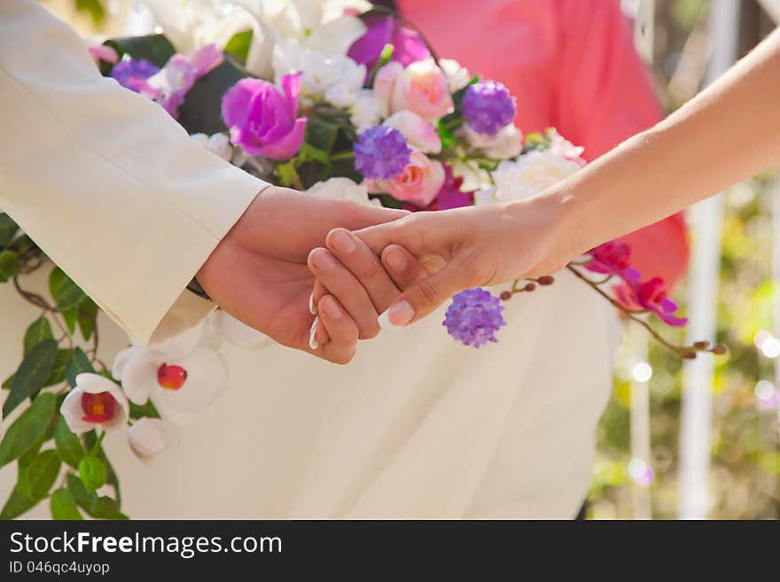 Holding hands during the wedding with floral background. Holding hands during the wedding with floral background
