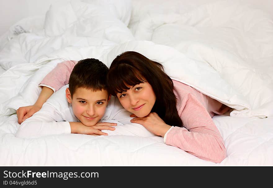 Mother hugging her son in bed smiling covered with white blanket. Mother hugging her son in bed smiling covered with white blanket