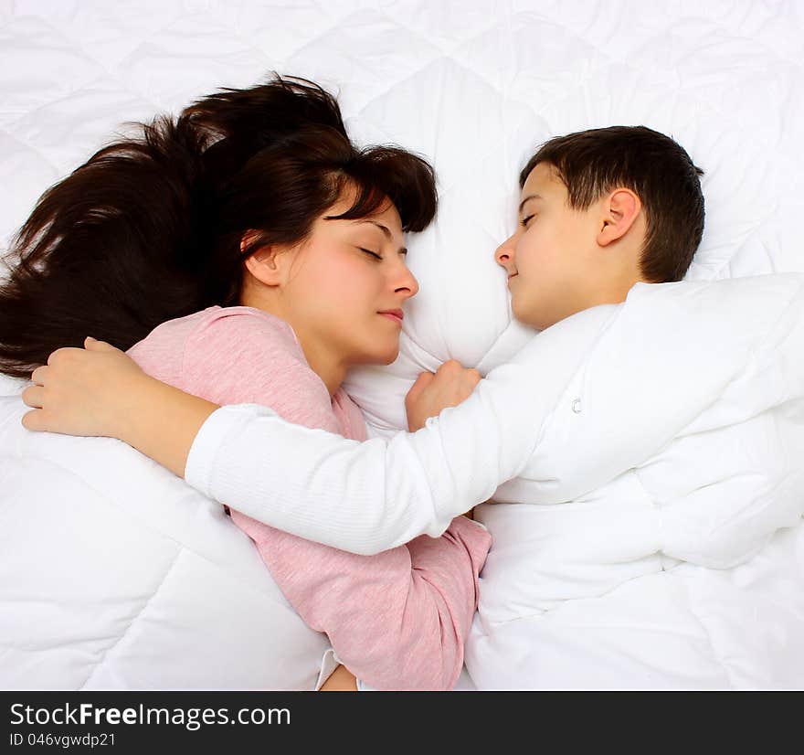 Mother and son sleeping covered with white blanket. Son hugging hes mother. Mother and son sleeping covered with white blanket. Son hugging hes mother