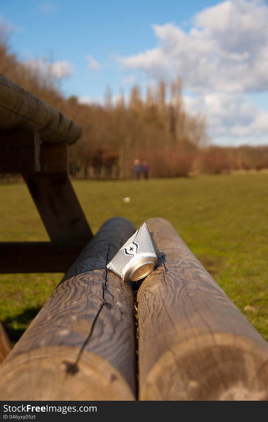 Discarded drinks can on a picnic bench at a parkland beauty spot. Two people walking away in the distance. Blue sky on a sunny day. Discarded drinks can on a picnic bench at a parkland beauty spot. Two people walking away in the distance. Blue sky on a sunny day.