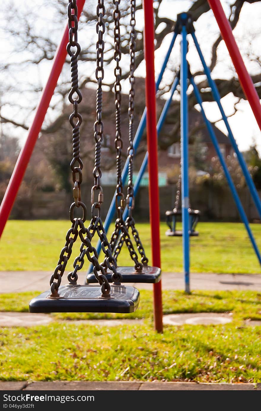 Row of childs swings in a playground setting.  Bright red and blue frames.  Nearest swings in sharp focus fading to toddler swings in distance. Row of childs swings in a playground setting.  Bright red and blue frames.  Nearest swings in sharp focus fading to toddler swings in distance.