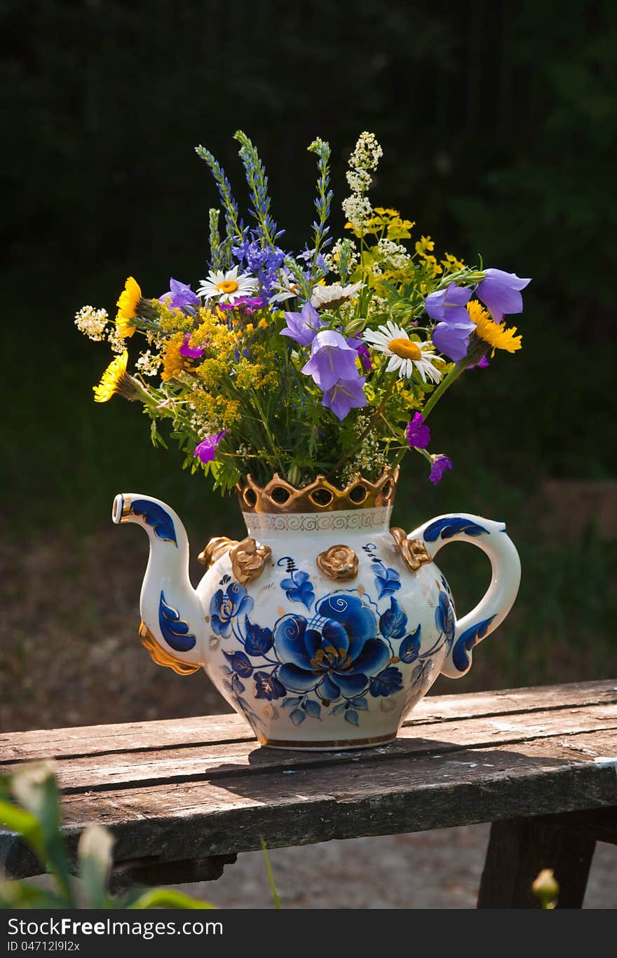 In the big teapot, painted with dark blue colours, a bouquet of wild flowers. In the big teapot, painted with dark blue colours, a bouquet of wild flowers