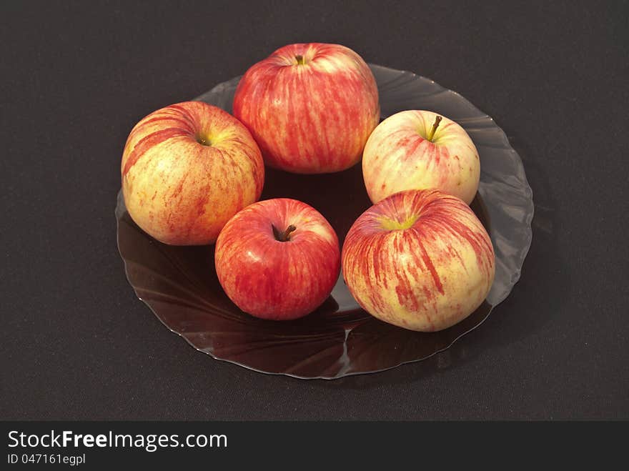 On a black background in a transparent plate five ripe apples. On a black background in a transparent plate five ripe apples.