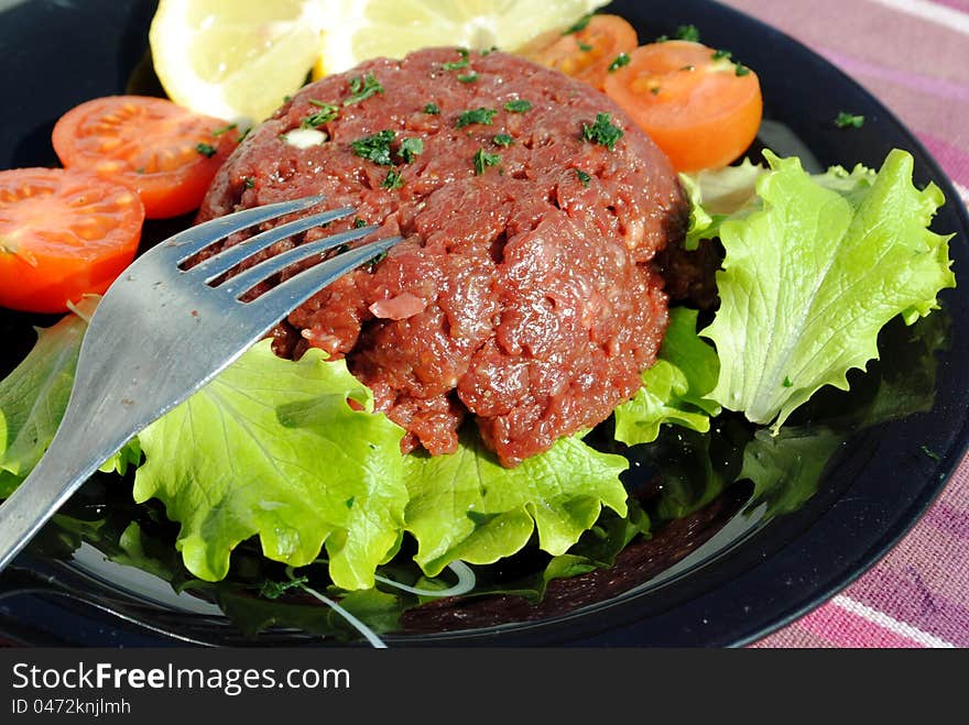 Raw ground beef with vegetables on a black dish