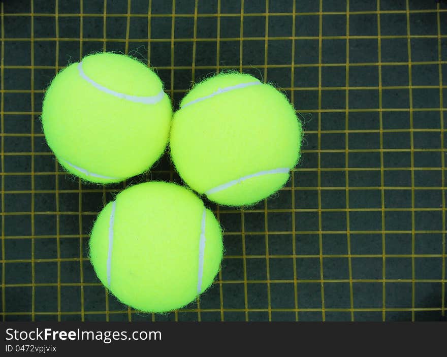 Three tennis balls placed on a racket strings in the background. Three tennis balls placed on a racket strings in the background