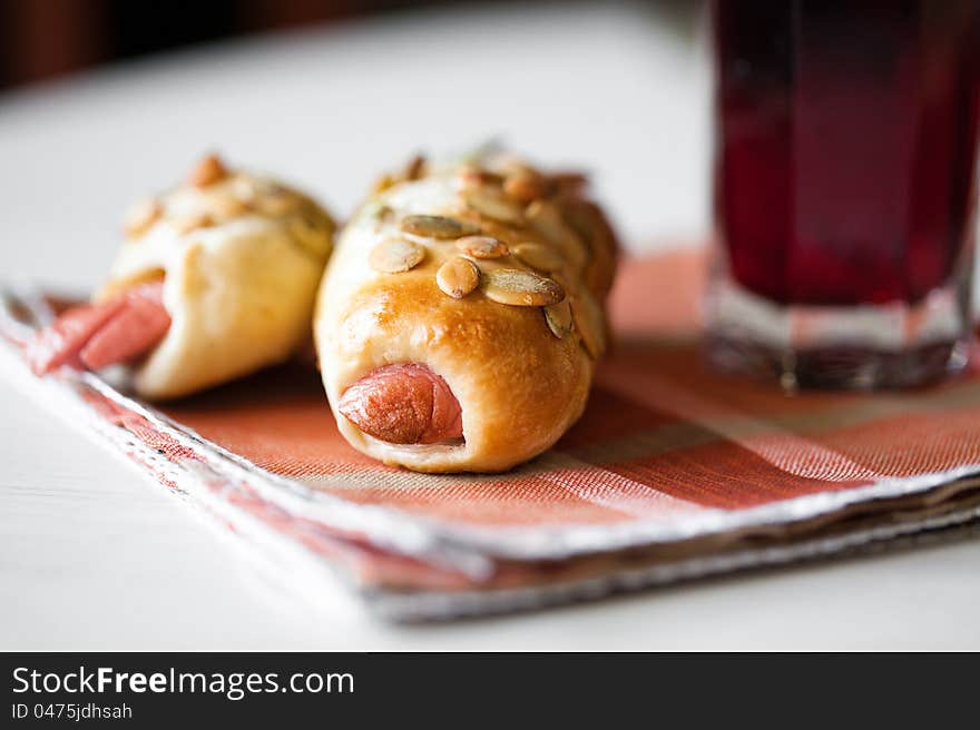 Two roll with sausage on the table and a glass of juice. Two roll with sausage on the table and a glass of juice