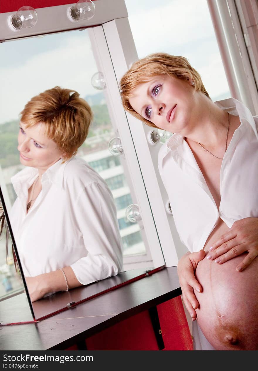 Beautiful pregnant woman daydreaming in front of a mirror