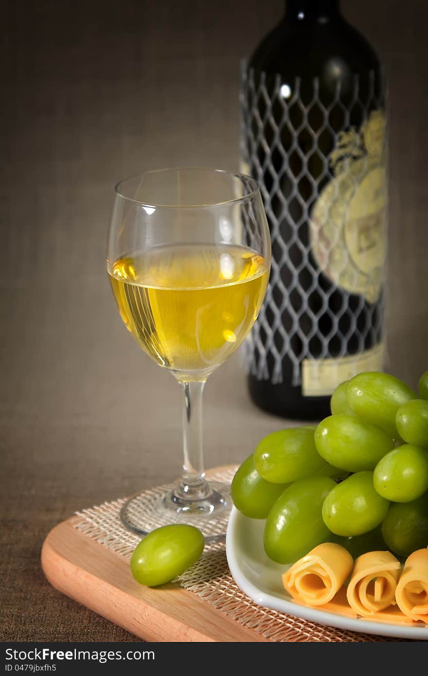 A glass of white wine, green grapes and a bottle of wine on a wooden surface