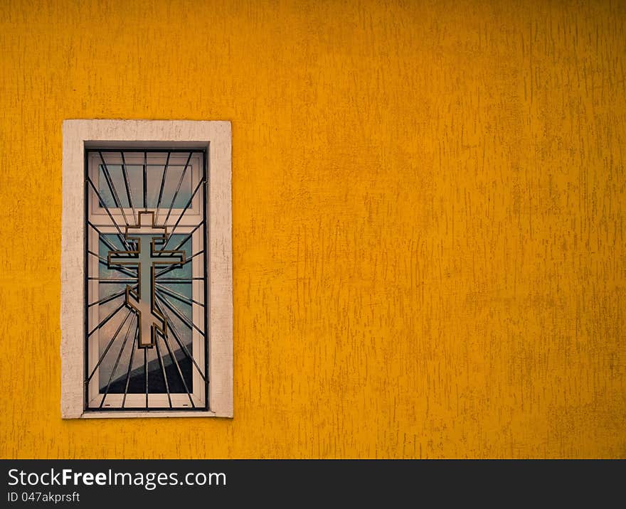 Window with grates and cross at yellow building wall