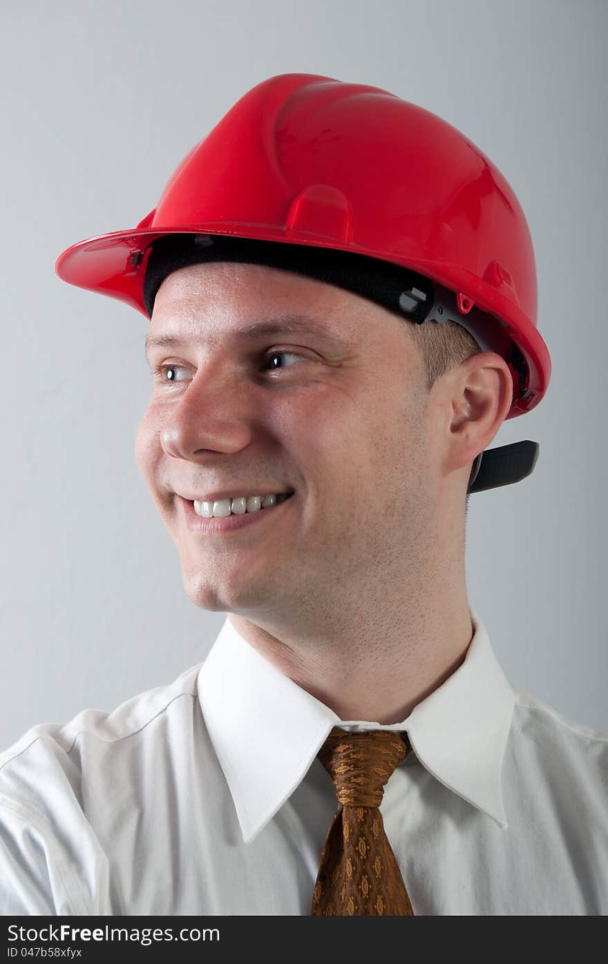 Portrait of young smiling engineer with red helmet on gray.