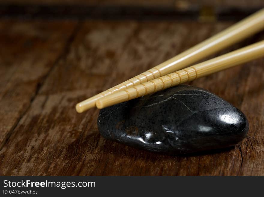 Close up of a pair of light chopsticks resting on a black stone on a rustic wood table. Close up of a pair of light chopsticks resting on a black stone on a rustic wood table.