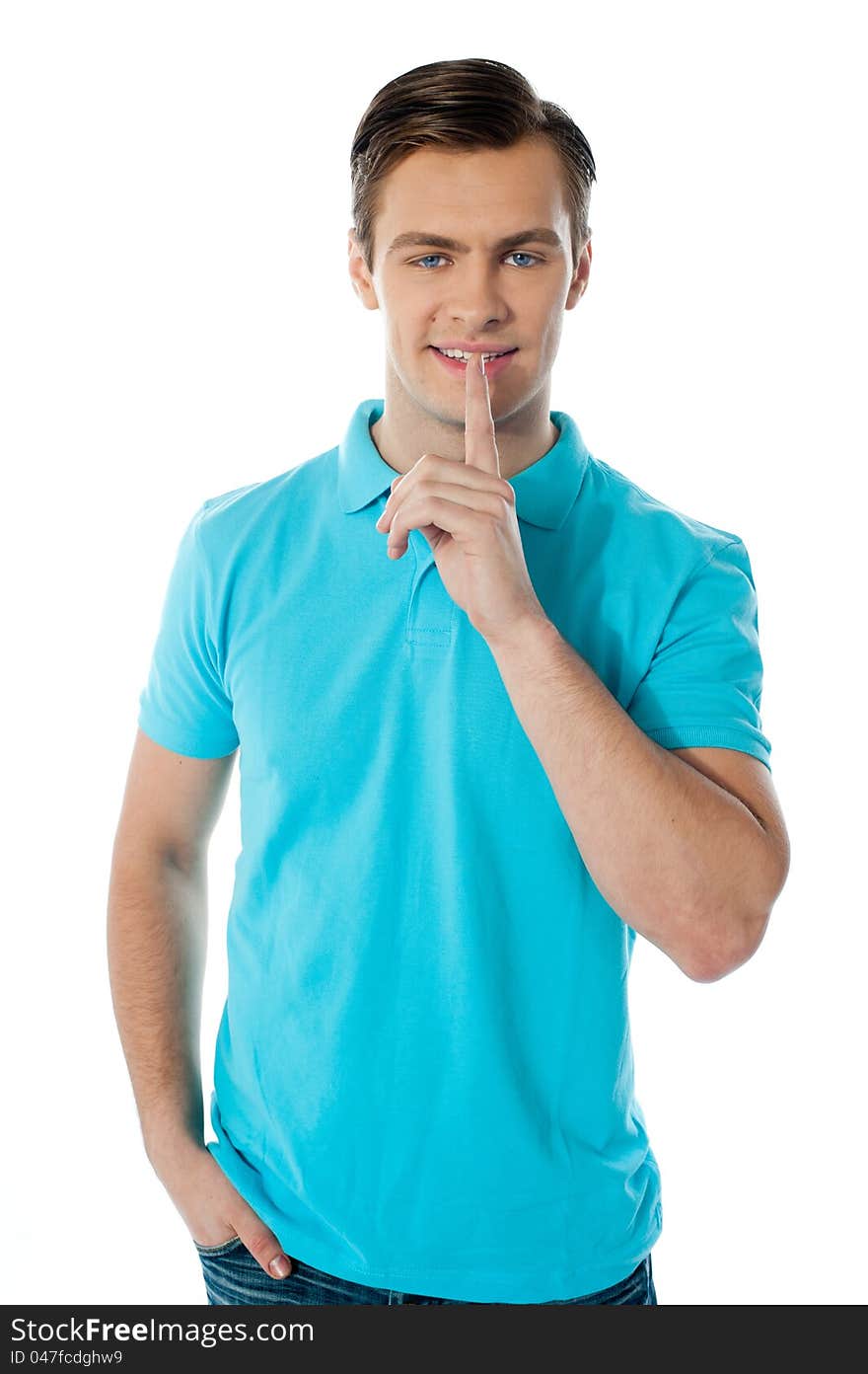 Silence gesture by a young guy wearing blue t-shirt against white background. Silence gesture by a young guy wearing blue t-shirt against white background