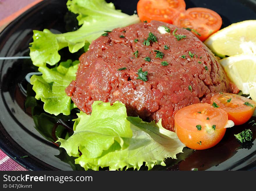 Raw ground beef with vegetables on a black dish