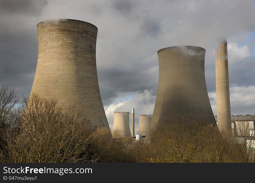 Giant cooling towers at an electricity generating station. White steam against a moody sky with winter sun. Giant cooling towers at an electricity generating station. White steam against a moody sky with winter sun.