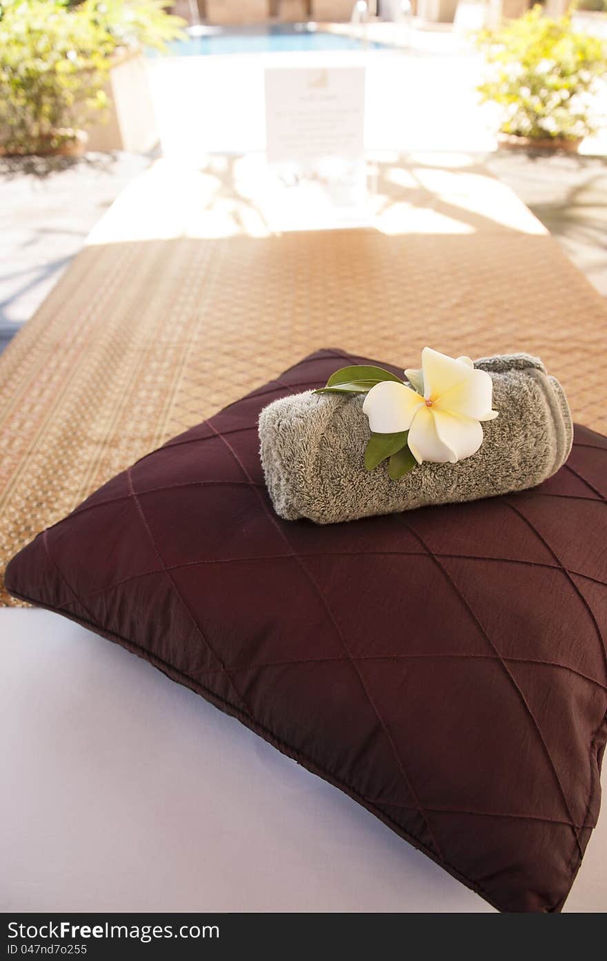 A bed near swimming pool with pillow and towel