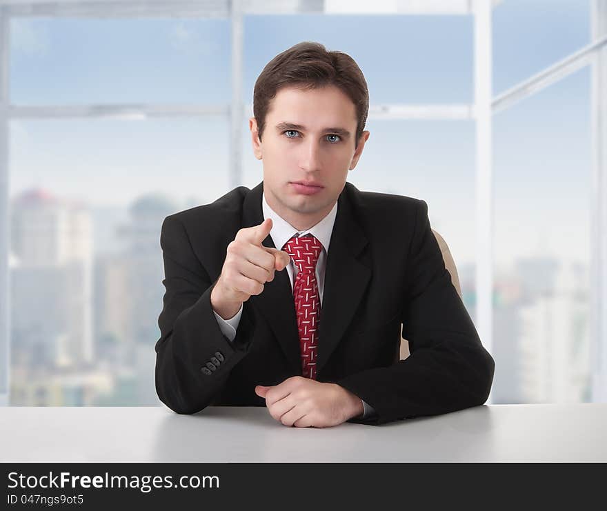 Successful businessman seriously sitting at a desk in his office and shows the index finger of the hand. Successful businessman seriously sitting at a desk in his office and shows the index finger of the hand