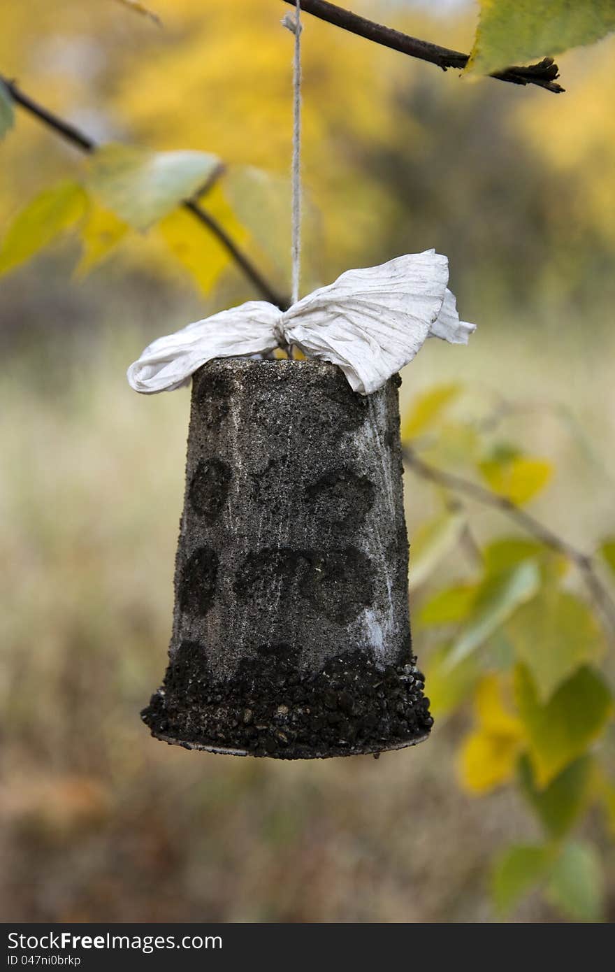 Stone bell with a paper ribbon, a bell hung on a branch, bell isolated from the background, yellow leaves in the background of the bell, handmade decorations