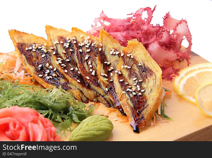 Sashimi tamago with slices of japanese omletn, lemon lobules, ginger wasabi, red and green algae on rectangular board isolated on a white background. Sashimi tamago with slices of japanese omletn, lemon lobules, ginger wasabi, red and green algae on rectangular board isolated on a white background