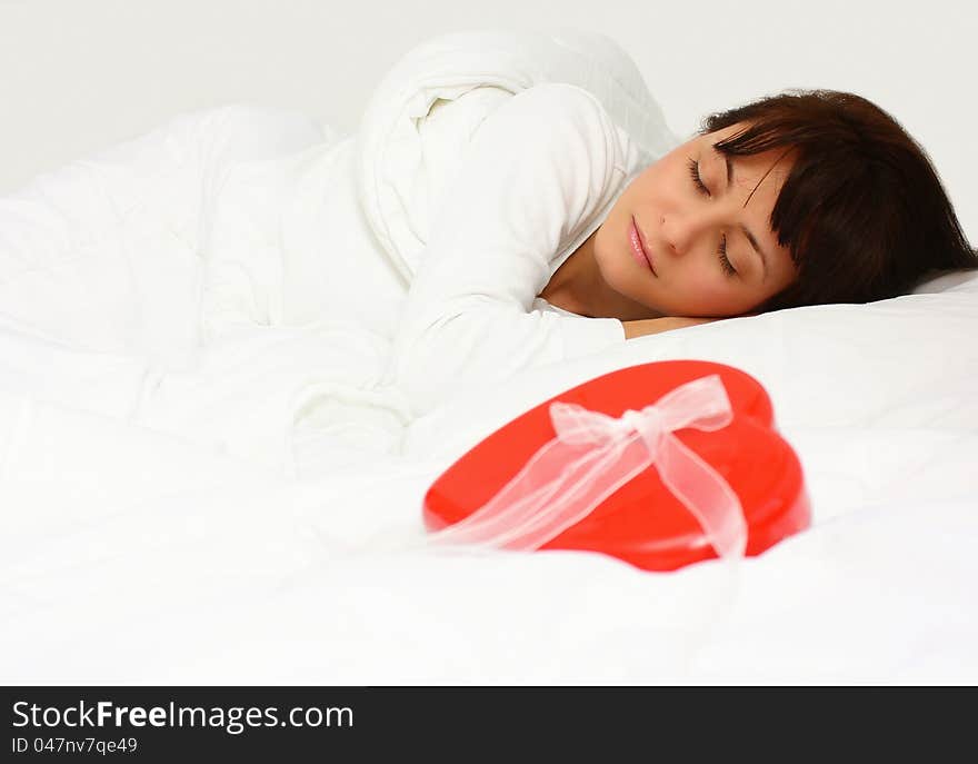 Beautiful woman sleeping in bed with a red gift heart shape next to her. Beautiful woman sleeping in bed with a red gift heart shape next to her