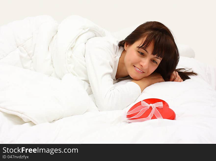 Surprised smiling woman finding a red gift with a heart shape in her bed in the morning