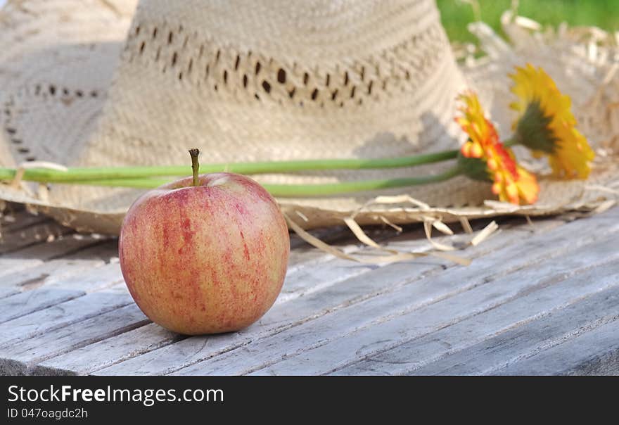 Apple placed front of  a straw hat in a garden in summer. Apple placed front of  a straw hat in a garden in summer